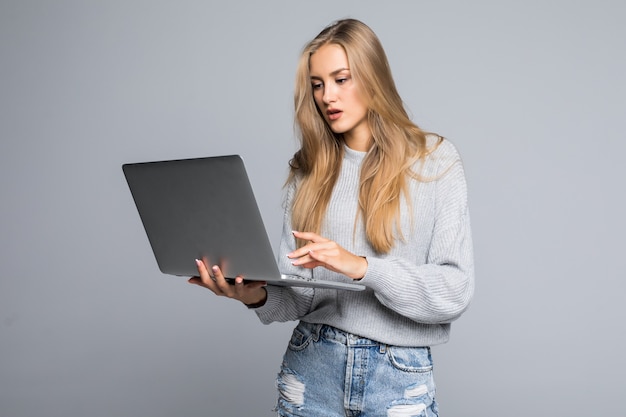 Young happy smiling woman in casual clothes holding laptop and sending email to her best friend isolated on gray background