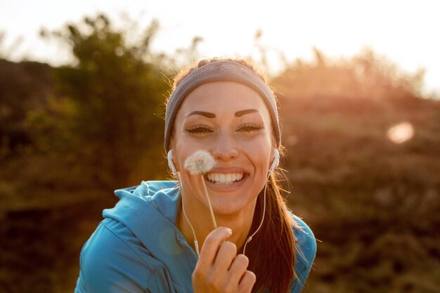 Young happy sportswoman holding dandelion flower in nature and looking at camera