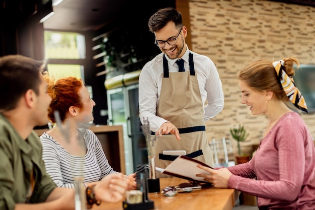 Free photo young happy waiter communicating with group of customers in a cafe