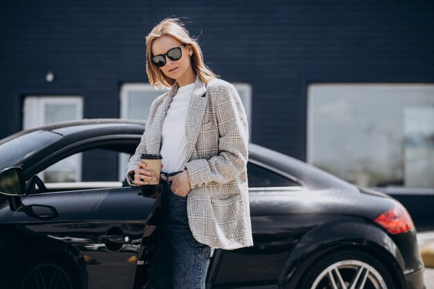 Young happy woman drinking coffee by the car