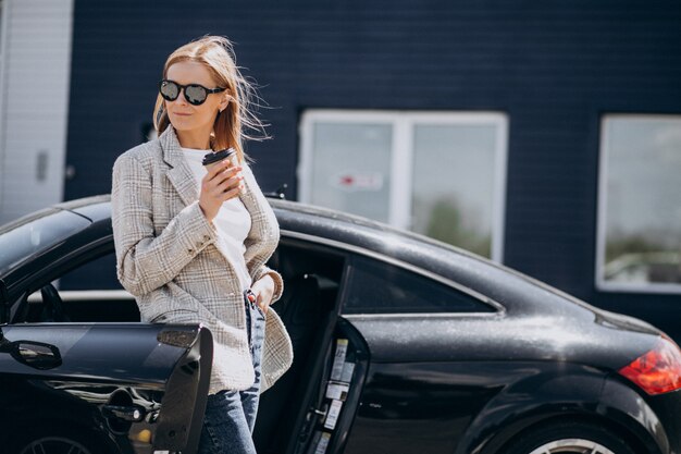 Young happy woman drinking coffee by the car