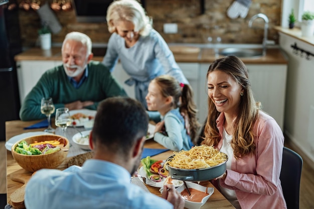 Free photo young happy woman laughing while passing food to her husband and enjoying in family lunch at dining table.