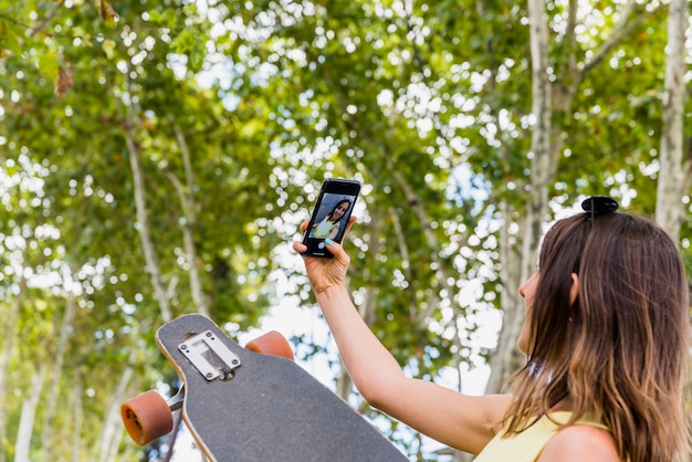 Free photo young happy woman with skateboard taking selfie