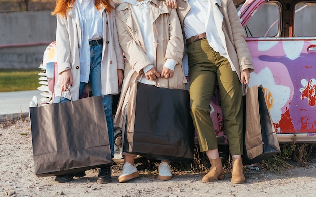 Young happy women with shopping bags posing near an old decorated car