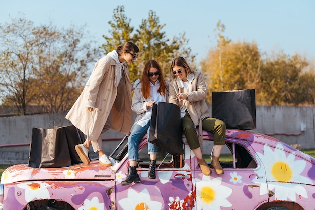 Young happy women with shopping bags posing near an old decorated car