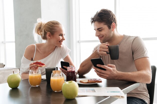 Young healthy couple using their smartphones while eating breakfast