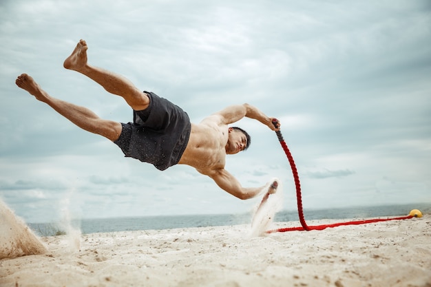 Free photo young healthy man athlete doing squats at the beach