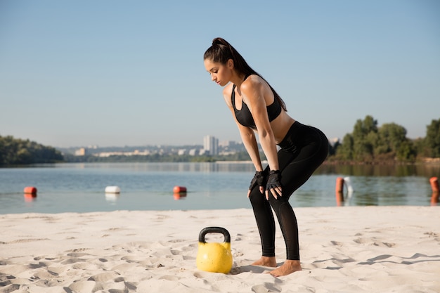 Free Photo young healthy woman doing squats with weights at the beach.