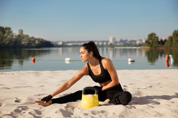 Young healthy woman stretching with weights at the beach.