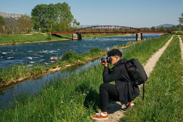 Free photo young hiker taking photo of idyllic river