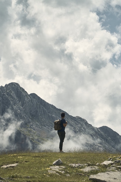 Free photo young hiker with a backpack surrounded by mountains under a cloudy sky in cantabria, spain