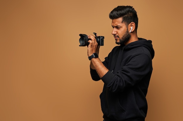 Young hindu photographer in black hoody with camera on wall