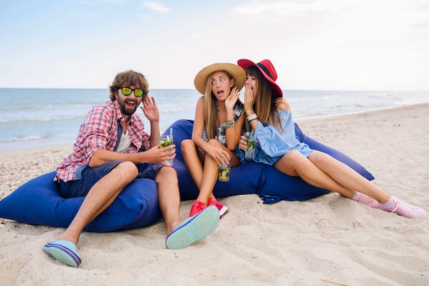 Young hipster company of friends on vacation sitting at beach on bean bags