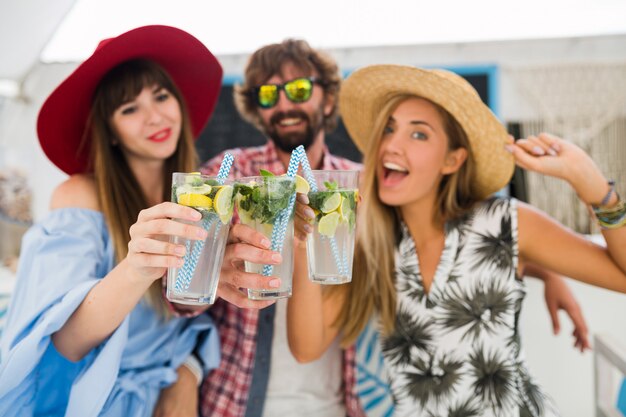 Young hipster company of friends on vacation at summer cafe, drinking mojito cocktails, happy positive style, smiling happy, two women and man having fun together, talking, flirt, romance, three