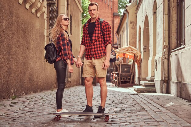 Young hipster couple, handsome skater and his girlfriend standing on the old narrow streets of Europe.