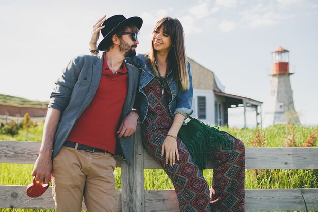 Young hipster couple indie style in love walking in countryside, lighthouse on background, summer vacation