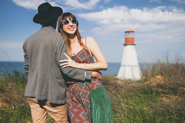 Young hipster couple indie style in love walking in countryside, lighthouse on background