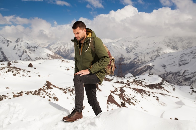 Young hipster man hiking in mountains, winter vacation traveling