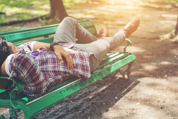 Free photo young hipster man lying down on green park bench, looking away.