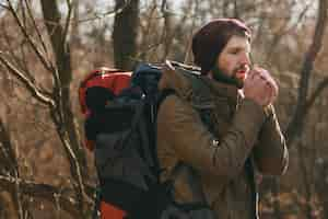 Free photo young hipster man traveling with backpack in autumn forest wearing warm jacket and hat