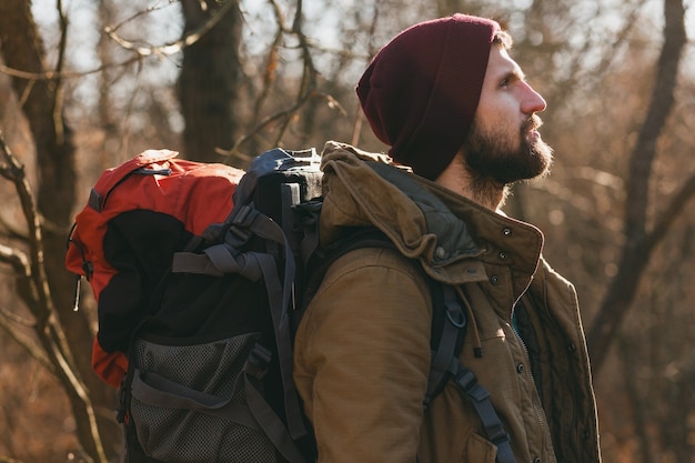 Free photo young hipster man traveling with backpack in autumn forest wearing warm jacket and hat