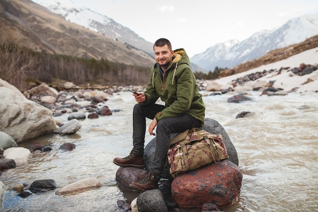 Young hipster man using smartphone, wild nature, winter vacation, hiking