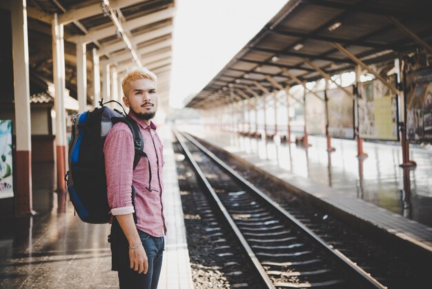 Young hipster man waiting on the station platform with backpack. Travel concept.