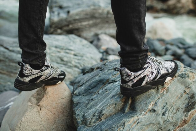 Young hipster man walking on a rock at river in winter forest