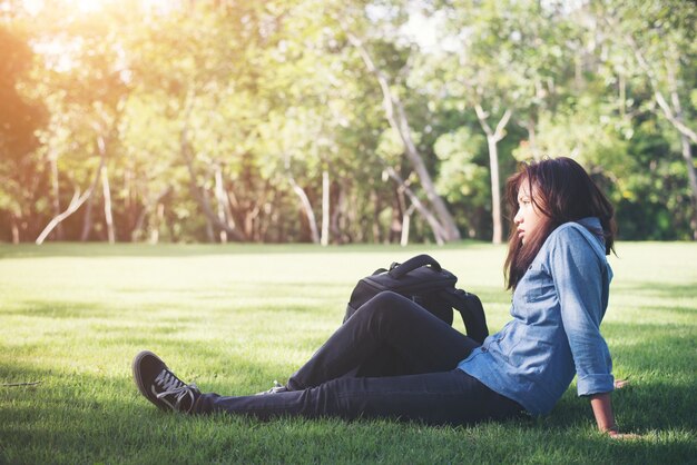 Young hipster woman lying down on green grass with backpack.