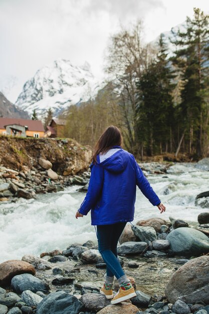 Young hipster woman walking on a rocks at river in winter forest