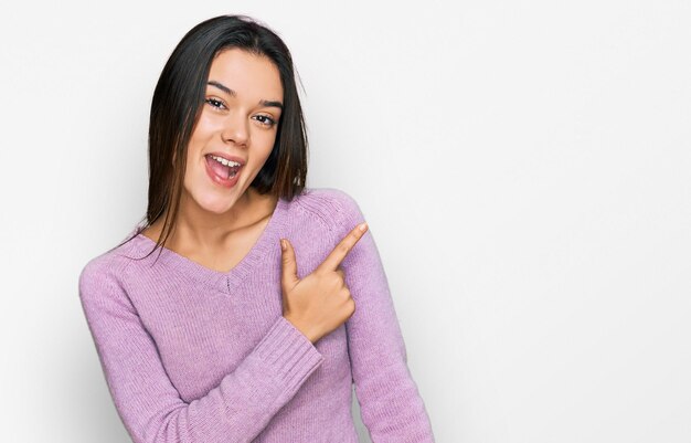 Young hispanic girl wearing casual clothes cheerful with a smile of face pointing with hand and finger up to the side with happy and natural expression on face