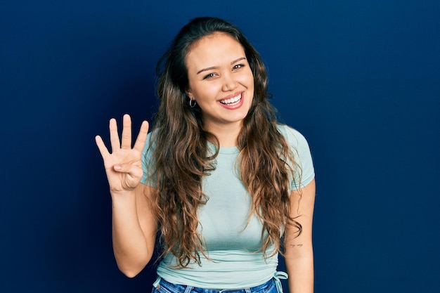 Free photo young hispanic girl wearing casual clothes showing and pointing up with fingers number four while smiling confident and happy.