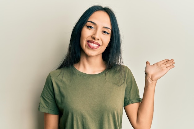 Free photo young hispanic girl wearing casual t shirt smiling cheerful presenting and pointing with palm of hand looking at the camera.