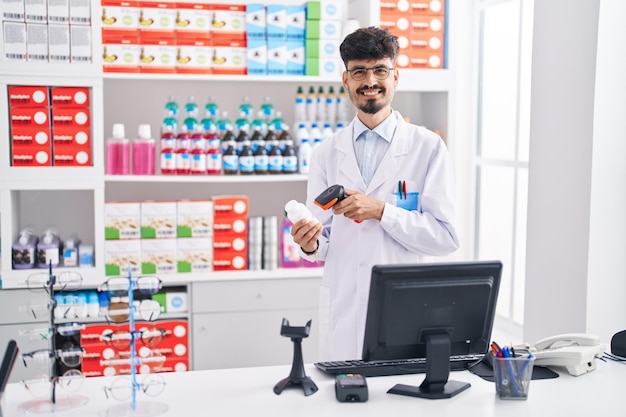 Free photo young hispanic man pharmacist smiling confident scanning pills bottle at pharmacy