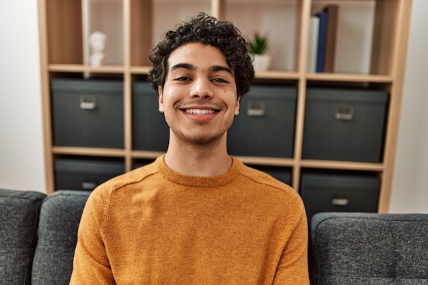 Young hispanic man smiling happy sitting on the sofa at home