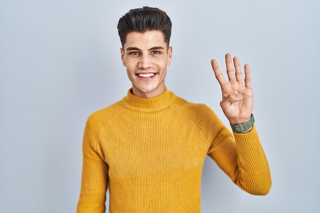 Young hispanic man standing over blue background showing and pointing up with fingers number four while smiling confident and happy