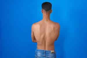 Free photo young hispanic man standing shirtless over blue background standing backwards looking away with crossed arms