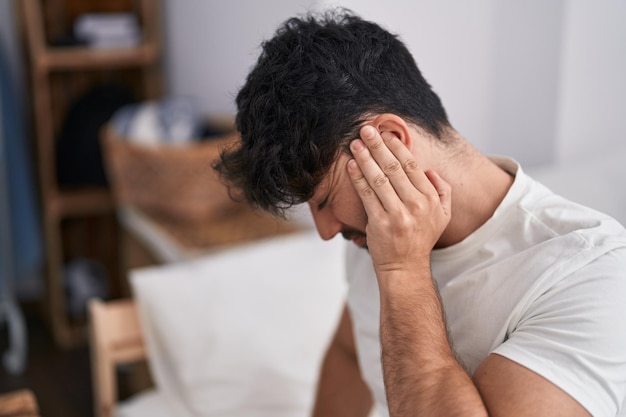 Young hispanic man suffering for backache sitting on bed at bedroom