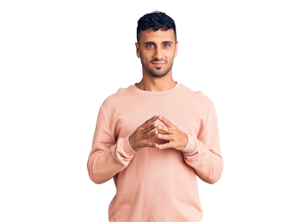 Young hispanic man wearing casual clothes hands together and fingers crossed smiling relaxed and cheerful. success and optimistic