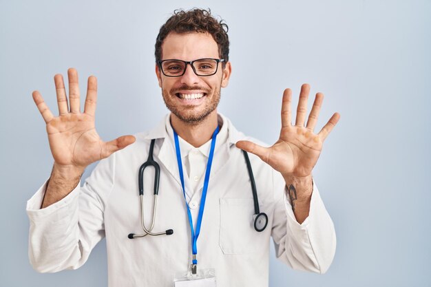 Young hispanic man wearing doctor uniform and stethoscope showing and pointing up with fingers number ten while smiling confident and happy.