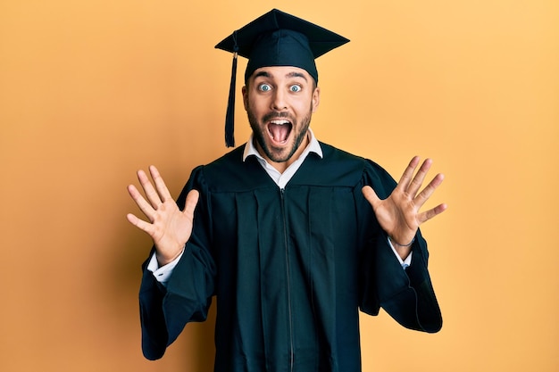 Free Photo young hispanic man wearing graduation cap and ceremony robe celebrating crazy and amazed for success with arms raised and open eyes screaming excited. winner concept