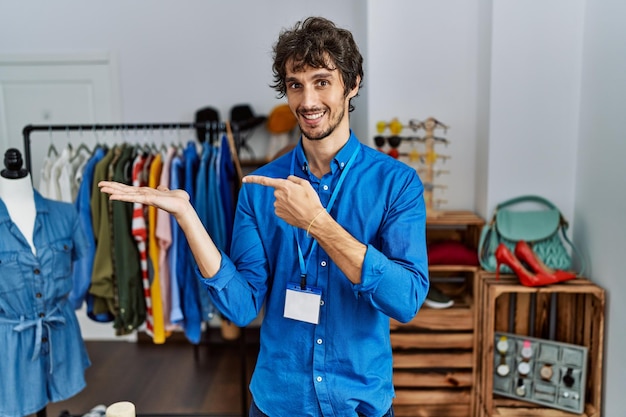 Young hispanic man working as manager at retail boutique amazed and smiling to the camera while presenting with hand and pointing with finger.