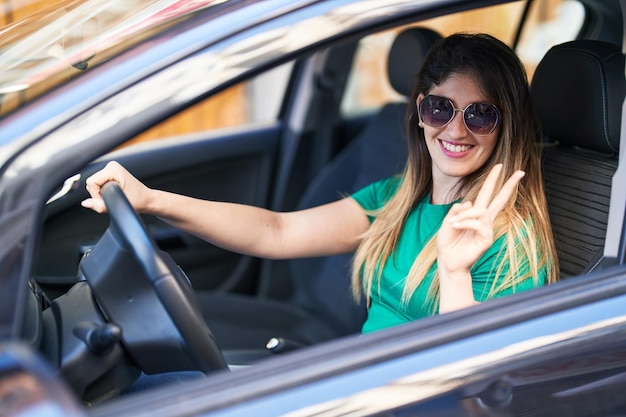 Free photo young hispanic woman doing victory gesture driving car at street