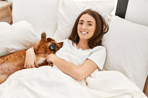 Free Photo young hispanic woman hugging dog lying on bed at bedroom