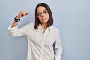 Free photo young hispanic woman standing over white background strong person showing arm muscle confident and proud of power