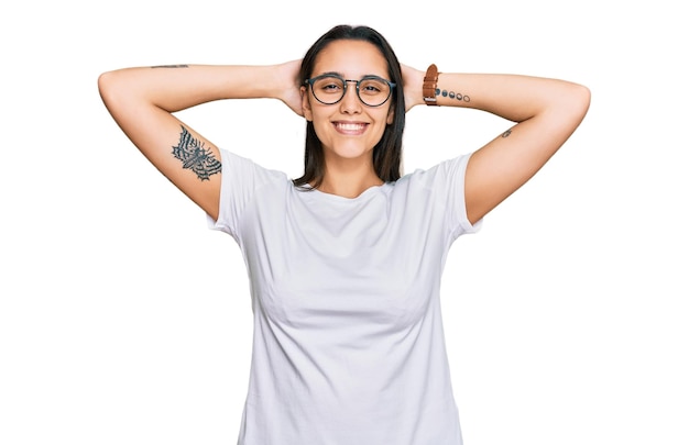 Free photo young hispanic woman wearing casual white t shirt relaxing and stretching, arms and hands behind head and neck smiling happy