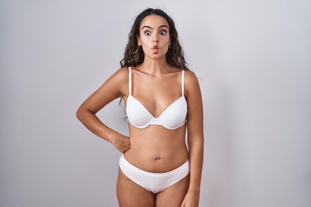 Young hispanic woman wearing white lingerie making fish face with lips, crazy and comical gesture. funny expression.