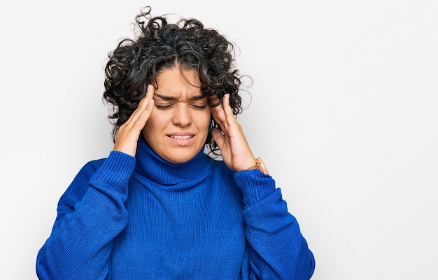 Free photo young hispanic woman with curly hair wearing turtleneck sweater with hand on head headache because stress suffering migraine