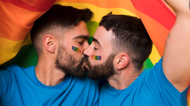 Young homosexual couple of men kissing on LGBT flag