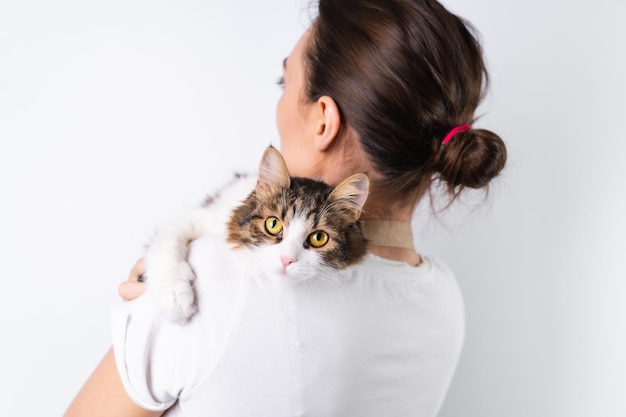 Free photo a young housewife in an apron on a white background holds her beloved pet a big fluffy cat a happy family